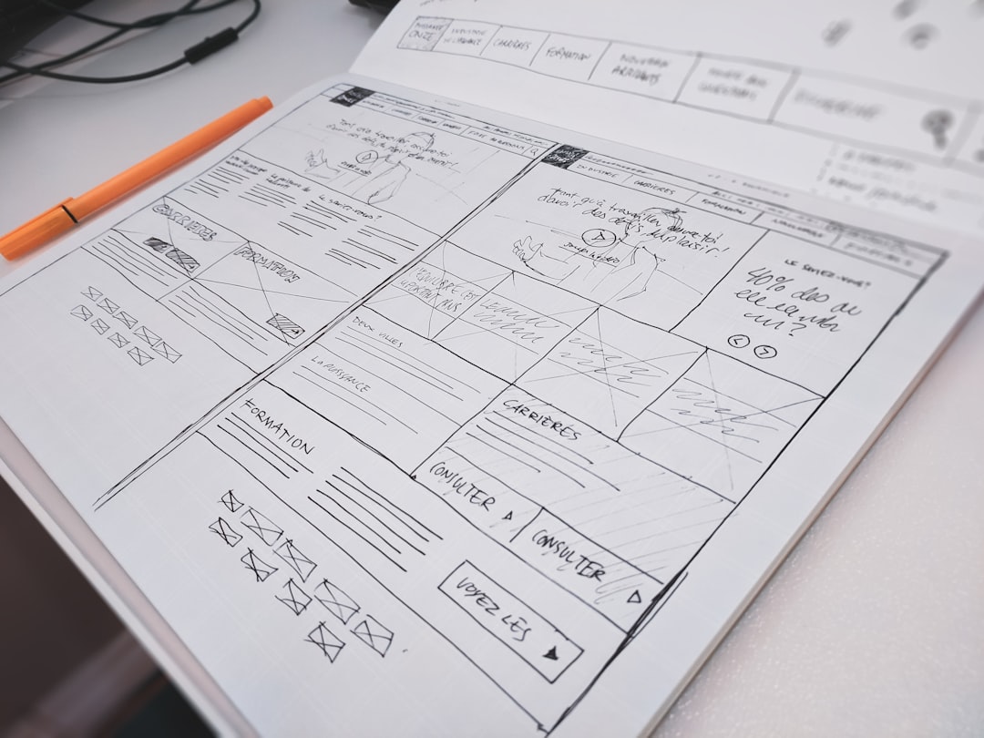 A hand-drawn website wireframe on paper with an orange pen on a desk