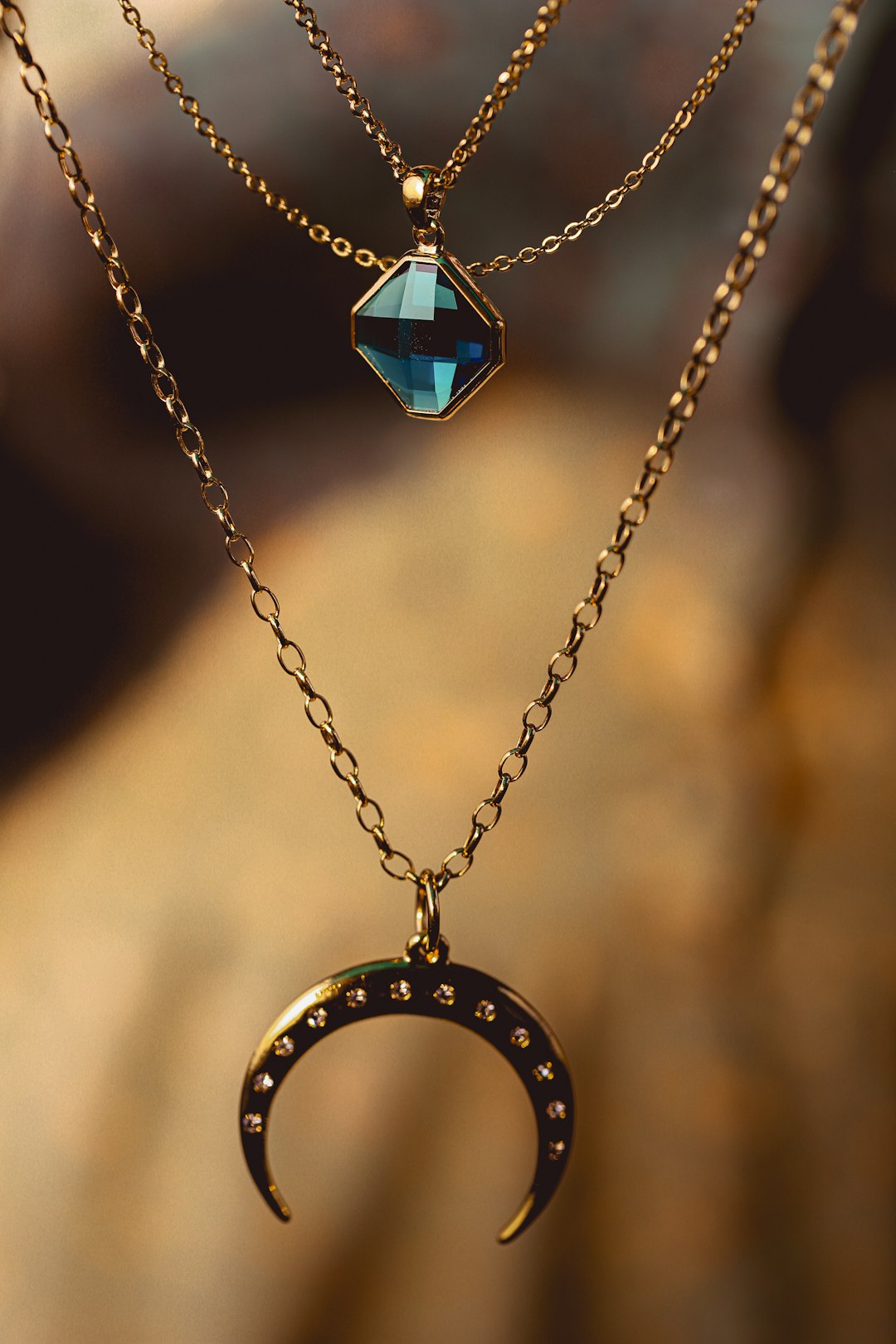 Two gold necklaces with a blue gemstone pendant and a crescent moon charm